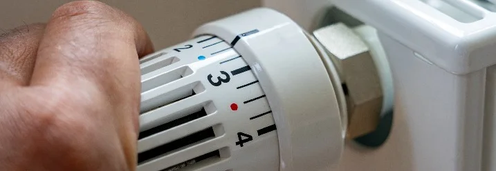 Hand dreht an einem Heizkörperthermostat